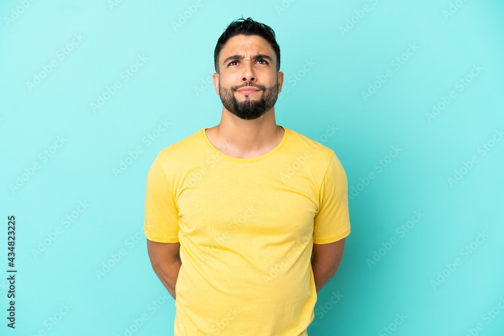 Young arab man isolated on blue background and looking up Young arab man isolated on blue background and looking up