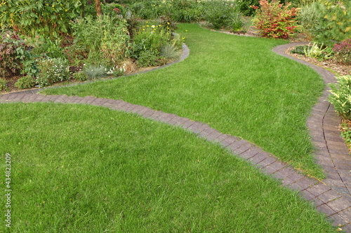 Backyard Garden Modern Design Landscaping. Landscaped Decorative Garden Winding Pathway Or Walkway From Black Bricks. Back Yard Lawn With Curved Brick Paving Path To Country House.