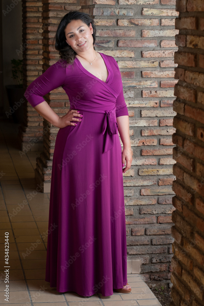 Hispanic latina model in a purple pink dress smiling and posing in location for a fashion portrait photoshooting  as a Mexican woman beauty concept