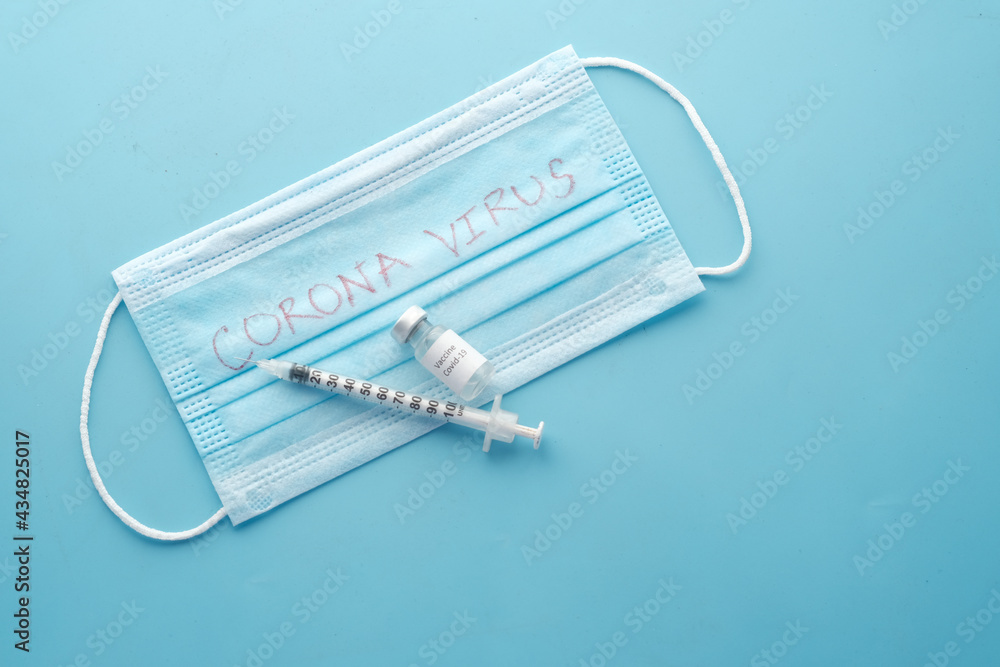 surgical face mask, coronavirus vaccine and syringe on blue background surgical face mask, coronavirus vaccine and syringe on blue background
