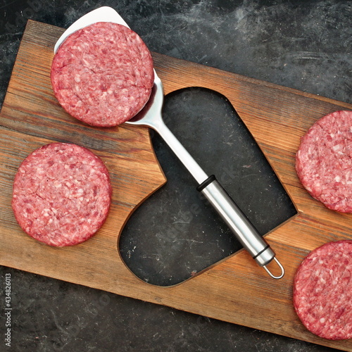 Patty of Minced Meat On Wooden Board with Shape of Heart. Raw Beef Steak Burgers on Wood Board with Heart Shape. Raw Steak Burgers Cutlets And BBQ Grill Tools Overhead View. Ground Beef Burgers.