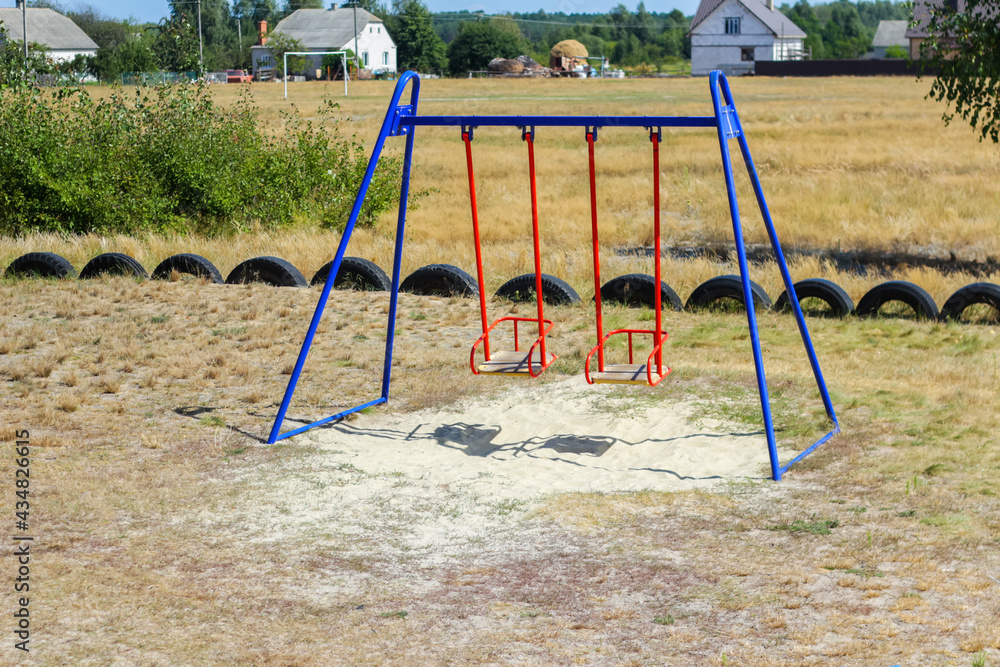 Fototapeta premium Defocus swing on playground on countryside area background. Bright blue and red swing. Family summer game. Out of focus
