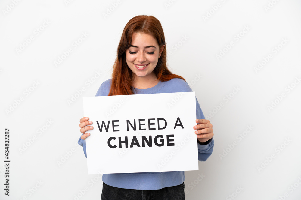 Young redhead woman isolated on white background holding a placard with text We Need a Change Young redhead woman isolated on white background holding a placard with text We Need a Change