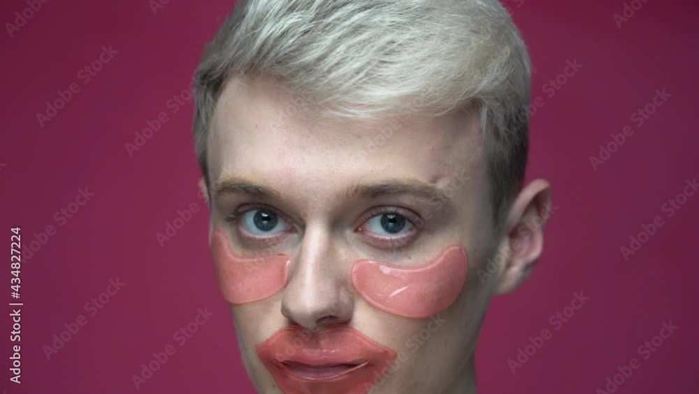 Close up of young transgender with lip and eye patches looking at mirror. Cosmetic procedure, skin care concept Close up of young transgender with lip and eye patches looking at mirror. Cosmetic procedure, skin care concept