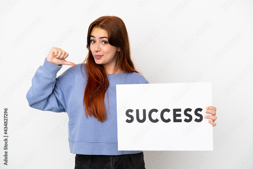 Young redhead woman isolated on white background holding a placard with text SUCCESS with proud gesture Young redhead woman isolated on white background holding a placard with text SUCCESS with proud gesture