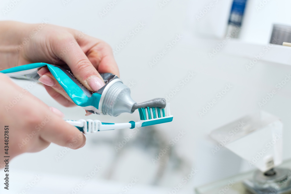 Squeezes toothpaste on toothbrush in bathroom blurred interior. Morning time, personal oral hygiene, prevention caries and dental care