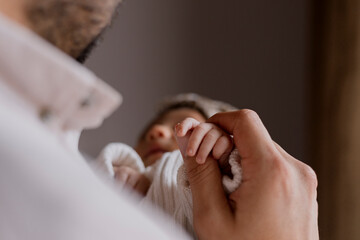 Close up of young father holding the hand of his newborn baby at home - Happy hispanic father holding his baby in his arms