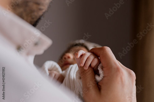 Close up of young father holding the hand of his newborn baby at home - Happy hispanic father holding his baby in his arms
