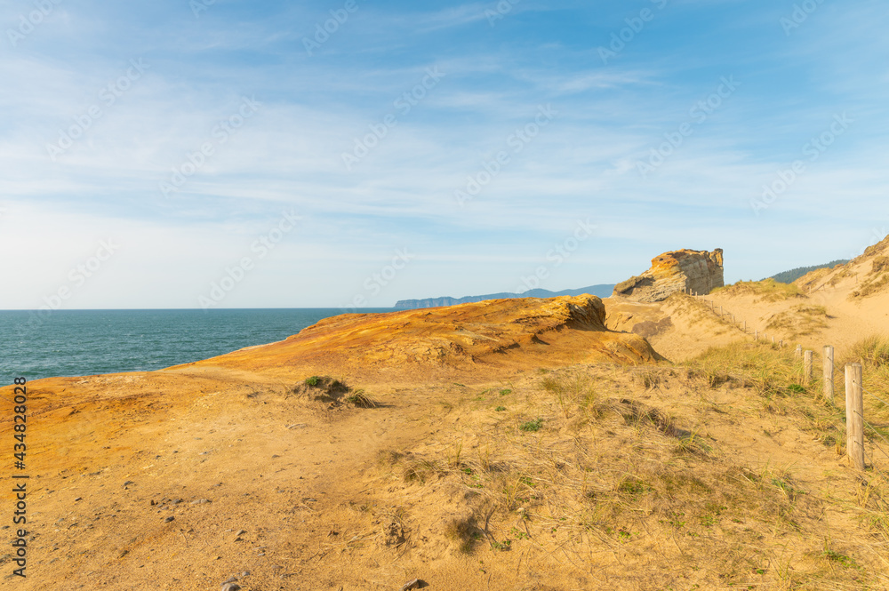 In the photo there is a yellow sandy mountain, a piece of the dark blue ocean, blue sky, light white clouds. No people. There is a place for your insert. Pastel shades. Daylight illumination.