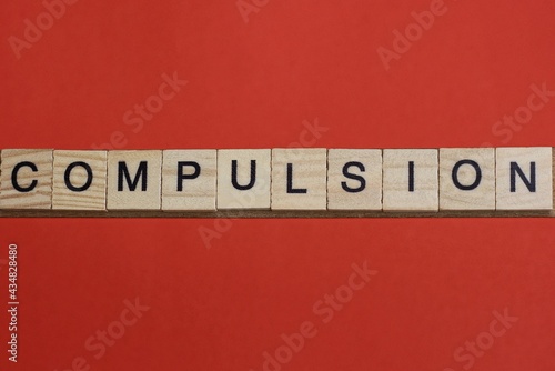 text the word compulsion from gray wooden small letters with black font on an red table