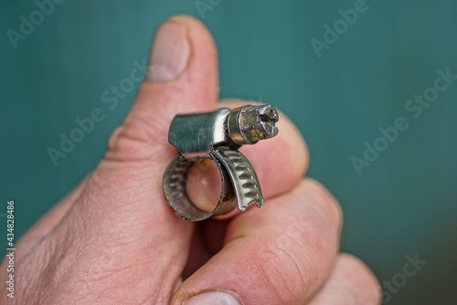 fingers hold one gray metal clamp with a bolt on a green background
