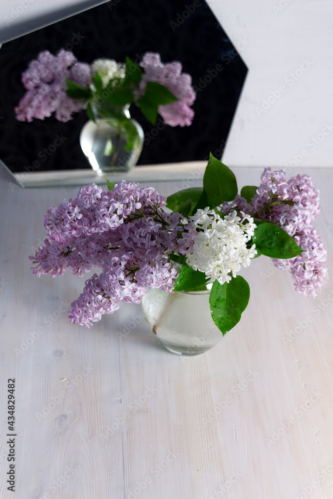 Fresh blooming purple and white lilac branches in glass vase reflecting in mirror Fresh blooming purple and white lilac branches in glass vase reflecting in mirror