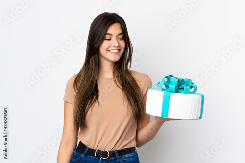 Teenager pastry chef holding a big cake over isolated white background with happy expression © luismolinero