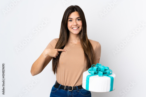 Teenager pastry chef holding a big cake over isolated white background with surprise facial expression © luismolinero