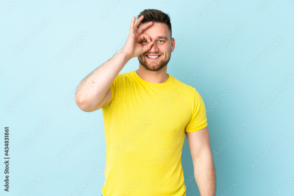 Russian handsome man isolated on blue background showing ok sign with fingers Russian handsome man isolated on blue background showing ok sign with fingers