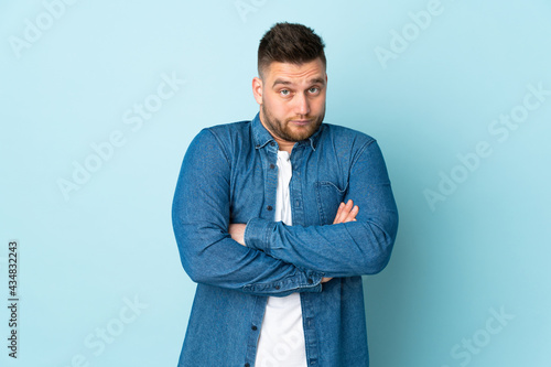 Russian handsome man isolated on blue background making doubts gesture while lifting the shoulders