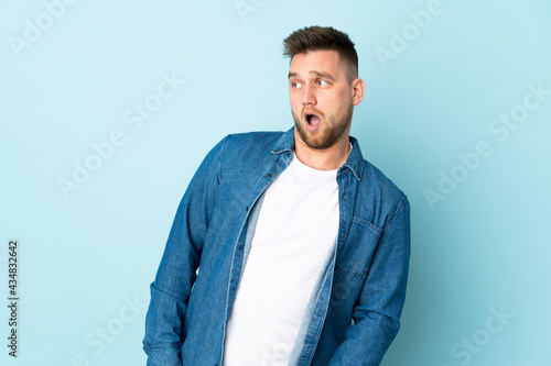 Russian handsome man isolated on blue background doing surprise gesture while looking to the side