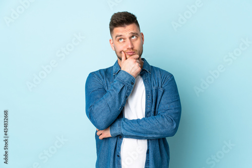 Russian handsome man isolated on blue background having doubts