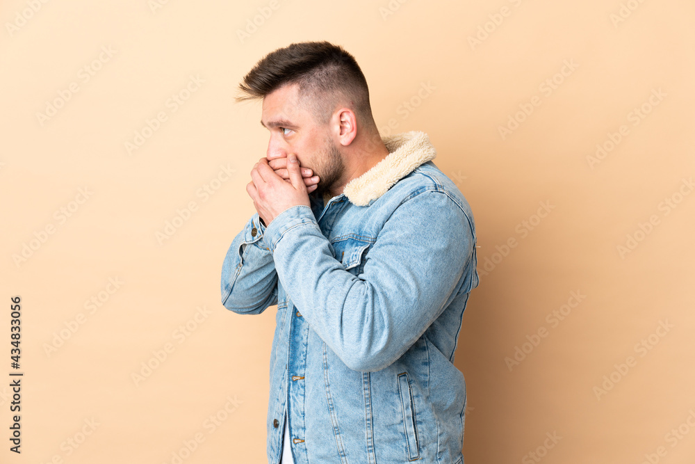 Russian handsome man over isolated background covering mouth and looking to the side Russian handsome man over isolated background covering mouth and looking to the side
