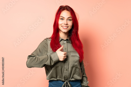Teenager red hair girl isolated on pink background giving a thumbs up gesture
