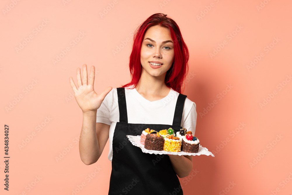 Pastry chef holding a muffins isolated on pink background counting five with fingers