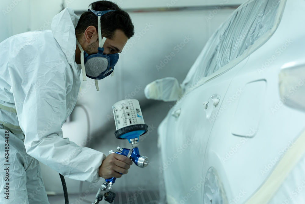 Young guy paints cars in his business for customers. Madrid