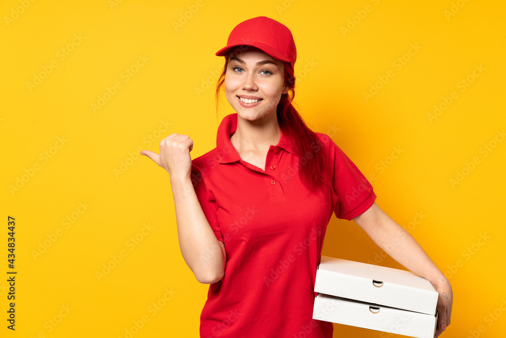Pizza delivery girl holding a pizza over isolated background pointing to the side to present a product Pizza delivery girl holding a pizza over isolated background pointing to the side to present a product