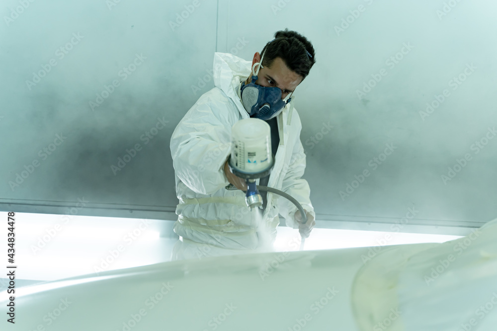 Dark-haired man paints the hood of a car in his own store. Madrid