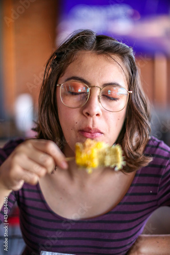 Young woman in retro style. Glasses and silk scarf. portrait  eating a corn. Charming happy girl with long hair smiling cheerfully