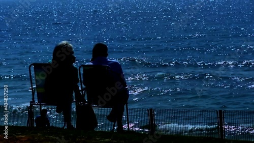 Elderly man and woman resting on folding chairs against the background of a slightly stormy sea at evening. HD