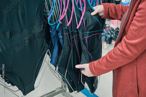 Caucasian woman chooses a black closed swimsuit to buy in a store. The concept of sports and active lifestyle. Hands close up shot