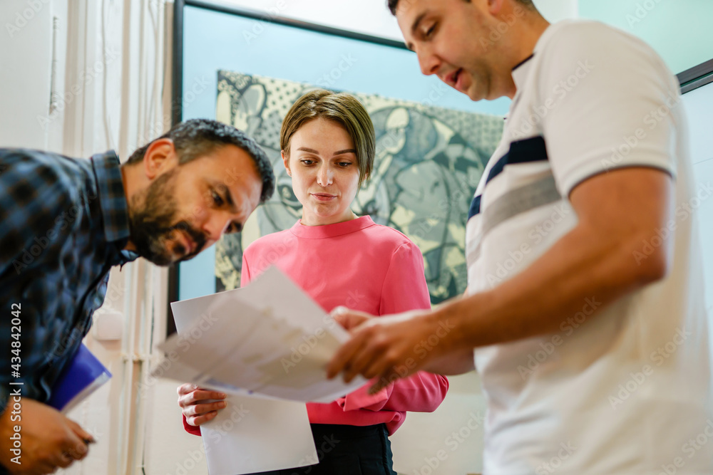 Adult caucasian woman standing in office with her male colleagues talking about business holding documents real people small business and entrepreneurs concept Adult caucasian woman standing in office with her male colleagues talking about business holding documents real people small business and entrepreneurs concept