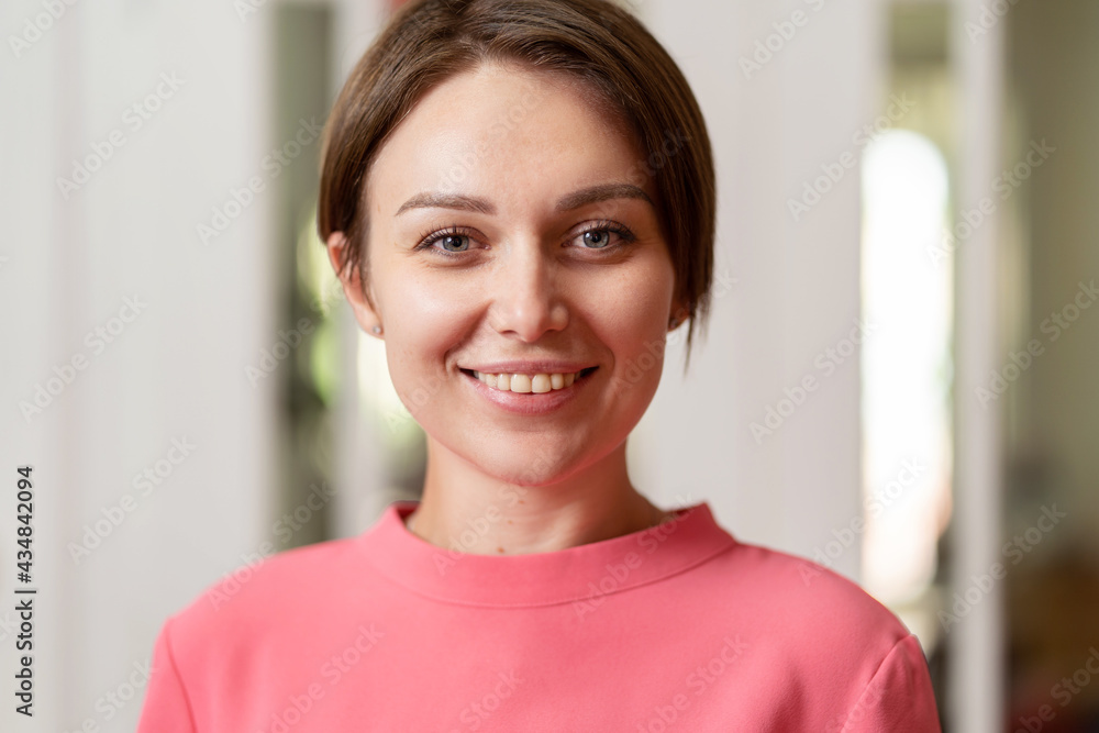 Front view portrait of happy smiling caucasian woman with short hair looking to the camera standing at office or home Front view portrait of happy smiling caucasian woman with short hair looking to the camera standing at office or home