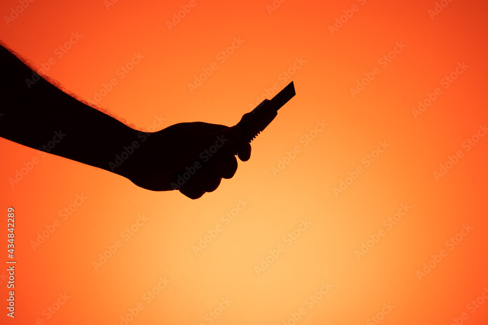Hand holding scalpel on orange background. Silhouette photography