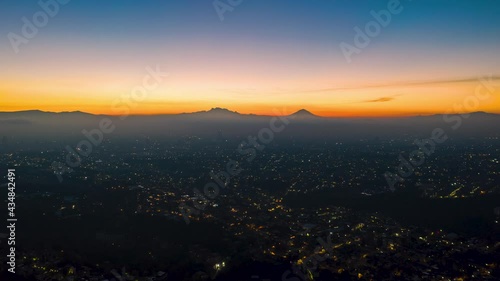 Aerial drone night to day hyperlapse of the business and financial district of Mexico City at sunrise, with skyscrapers and the cityscape. Popocatepetl active volcano in the background