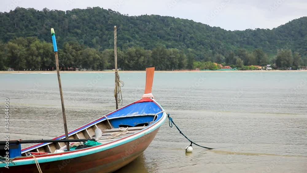 Thai longtail boat anchored along the beach by rope on the island of Koh Lanta in Thailand with water and waves. Thai longtail boat anchored along the beach by rope on the island of Koh Lanta in Thailand with water and waves.