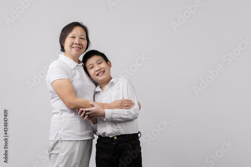 Portrait of Grandmother and grandchild hugging, looking at camera and smiling, on gray background