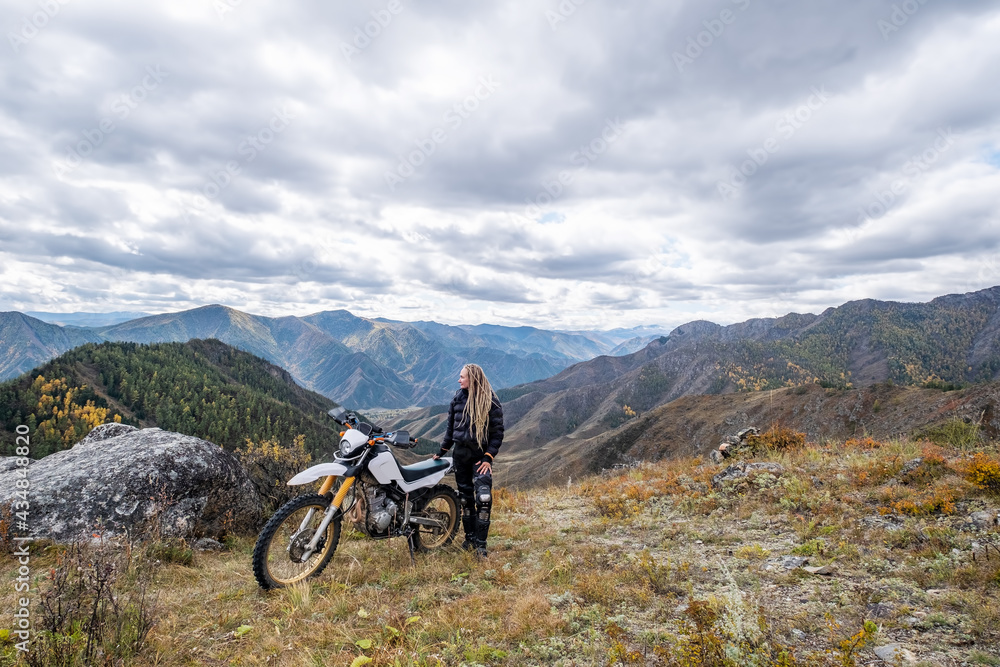 Young woman motorcyclist enjoying and rest on the mountain top with her enduro motorcycle. Off road motor traveling in wild mountains
