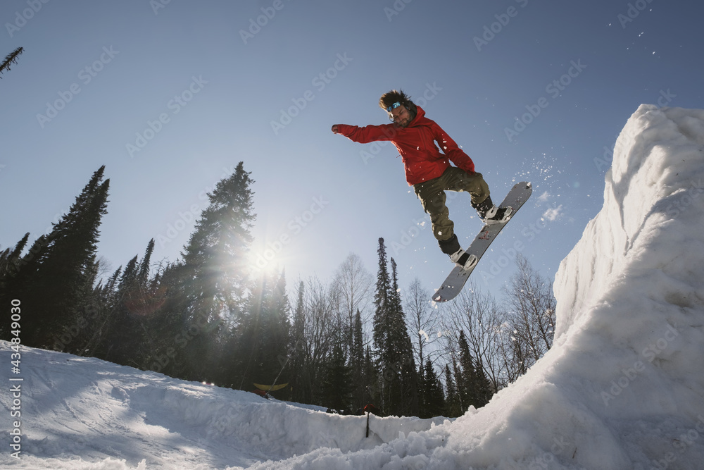 Snowboarder male jumping on quarter pipe snowboard in winter sunny day. Freestyle snowboard training