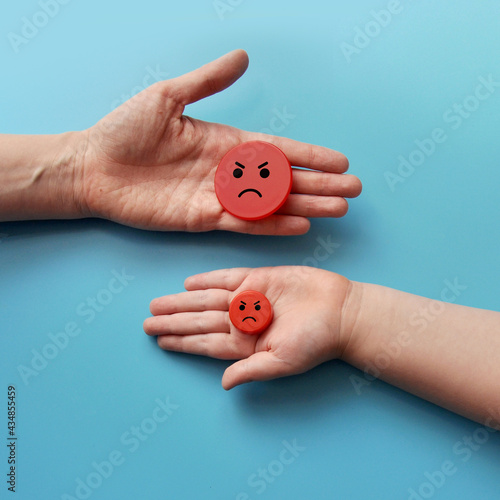 Mugs with angry faces in the hands of a child and an adult. Negative and positive emotions of the child. A symbol of negativity in the family, mother and child are angry at each other