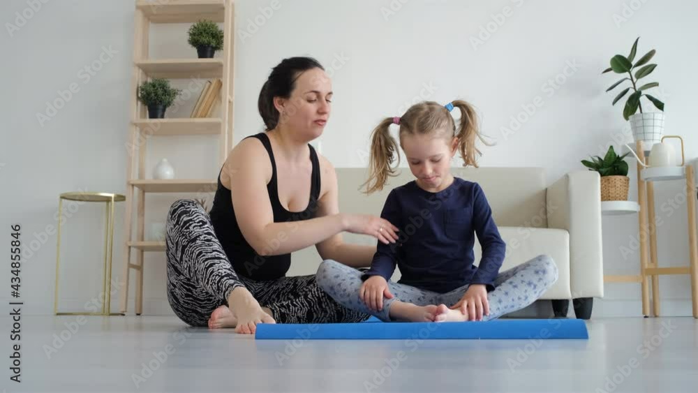Woman Training on a Mat with her Little Daughter at Home, Mother Helping Daughter with Exercises. Slow Motion. Healthy Lifestyle and Family Sport Activities Concept Woman Training on a Mat with her Little Daughter at Home, Mother Helping Daughter with Exercises. Slow Motion. Healthy Lifestyle and Family Sport Activities Concept