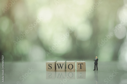 Miniature people businessman standing with wood word SWOT. SWOT Analysis Concept.