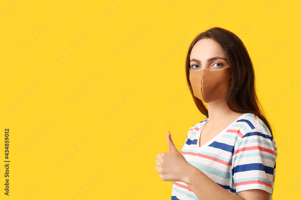 Young woman wearing medical mask and showing thumb-up on color background Young woman wearing medical mask and showing thumb-up on color background