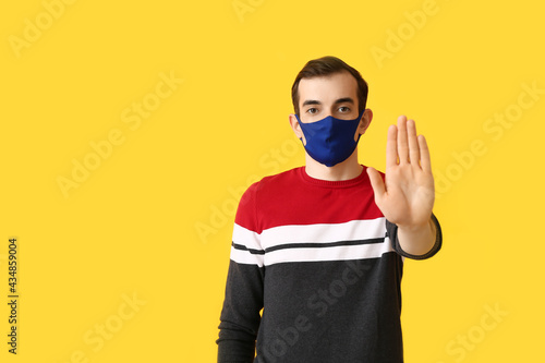 Young man wearing medical mask and showing STOP gesture on color background