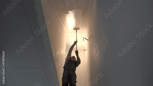 man painting gypsum plaster ceiling in staircase with painting roller
