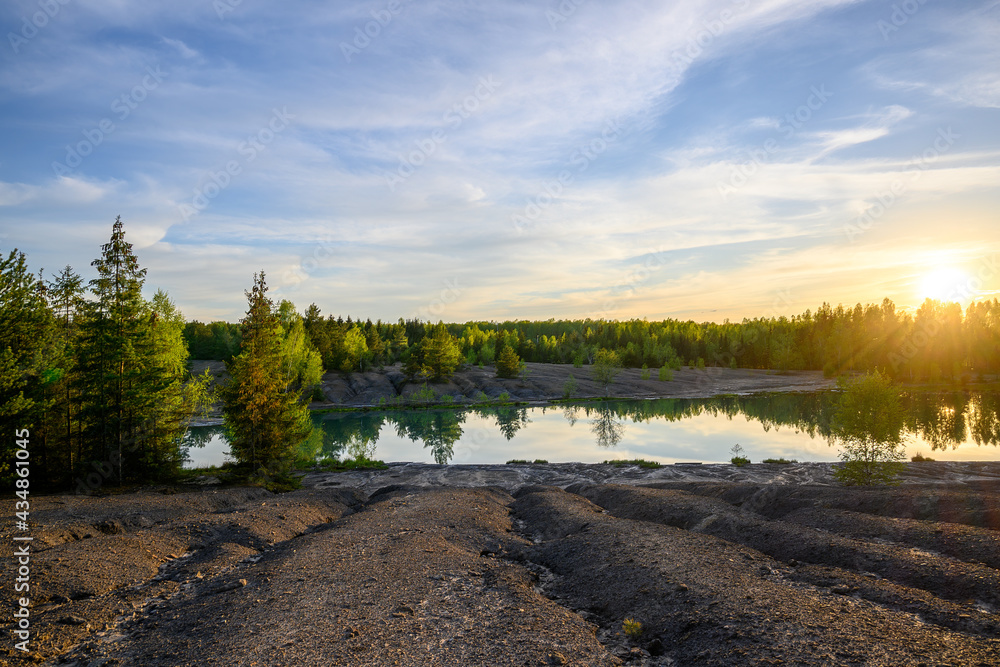 Beautiful sunset on the lake in springtime. Eroded ground in the foreground, birches and pine trees in the background. Setting sun colors clouds in bright colors.