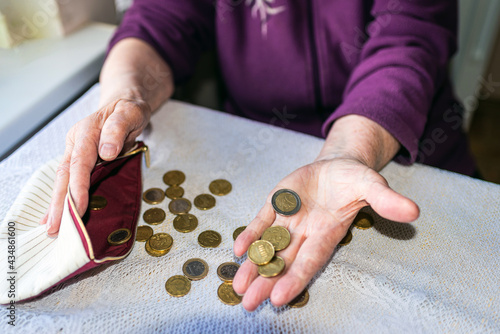 Old woman sitting miserably at home and counting remaining coins from the pension in her wallet after paying the bills. photo