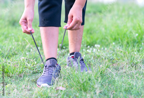Young fitness woman tie shoelace of sport shoes on the lawn.