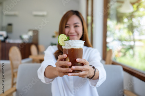 Portrait image of a beautiful young asian woman holding and serving a glass of iced coffee