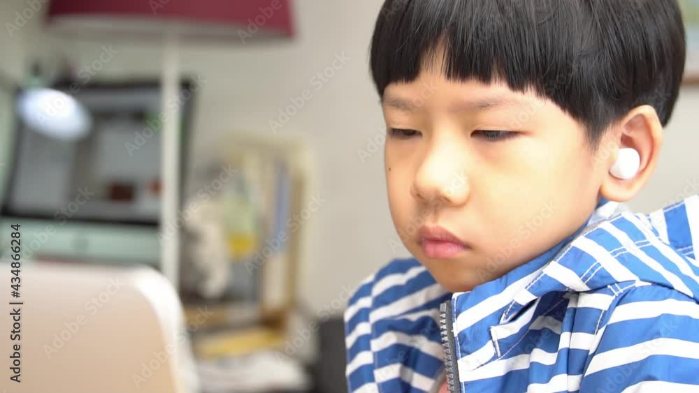 Online learning programs concept. Portrait of a cute and smart asian student boy with wireless earbuds using tablet computer to join online classroom from home during Covid-19 pandemic. New normal. Online learning programs concept. Portrait of a cute and smart asian student boy with wireless earbuds using tablet computer to join online classroom from home during Covid-19 pandemic. New normal.